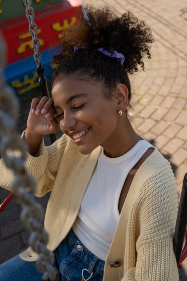 Cute black teenage girl sitting in carousel seat with eyes closed and smiling